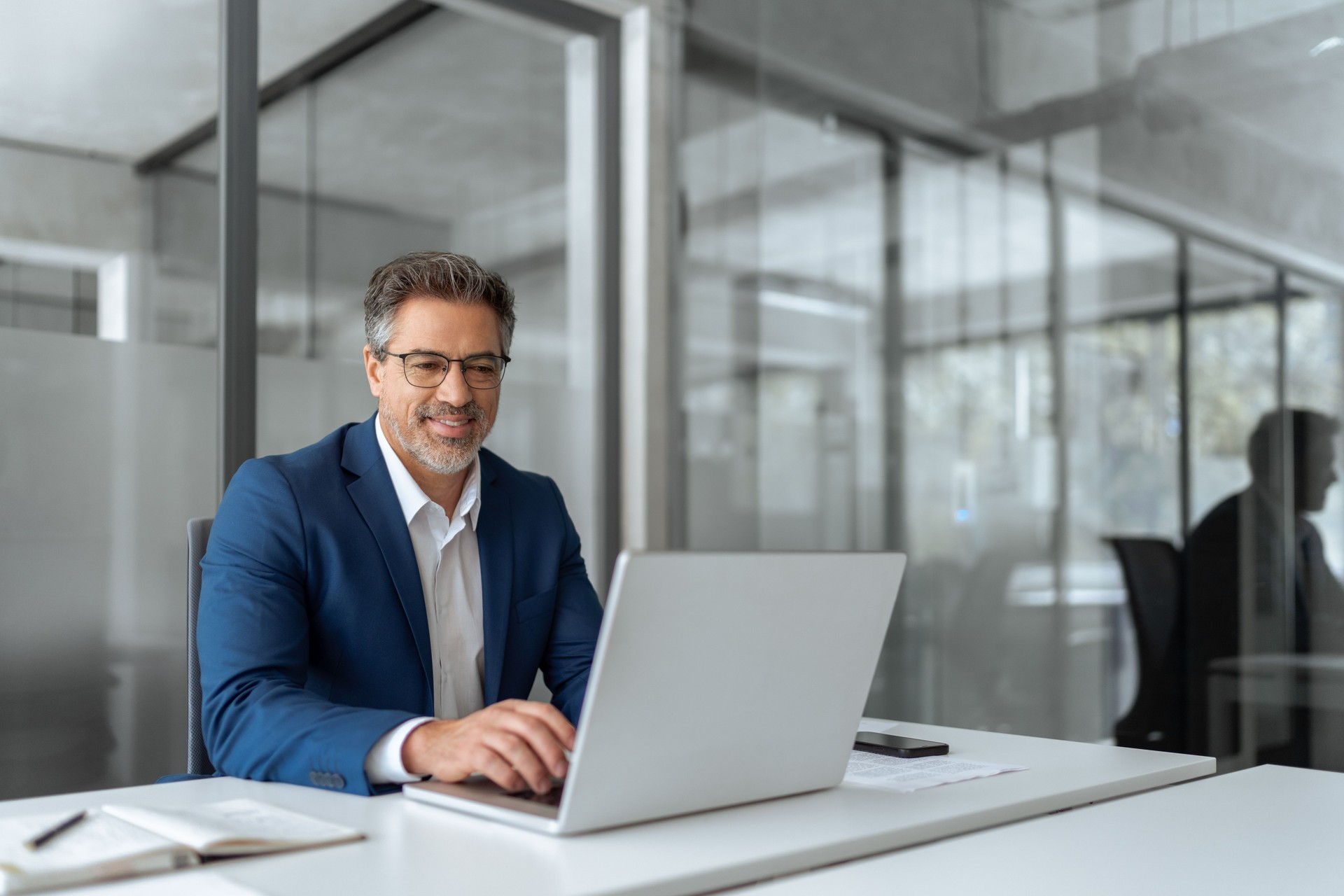 Mature Latin business man ceo manager using laptop computer in modern office. Smiling senior businessman entrepreneur sitting at desk working on finance work, looking thinking at screen. Copy space